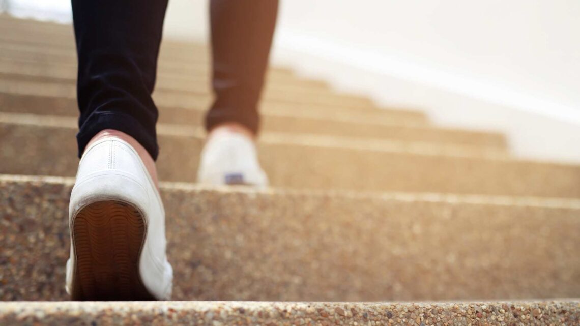 view from bottom of staircase, person with white running shoes taking a step up from the bottom. image is from the ankles down.