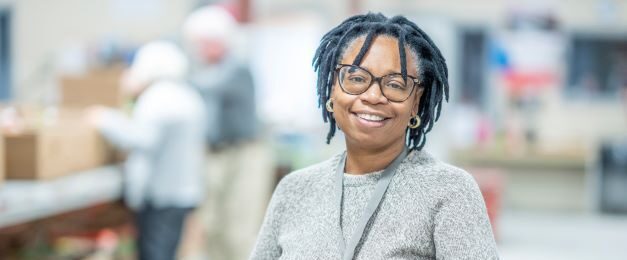 woman holding a cardboard box, smiling as she volunteers at food program