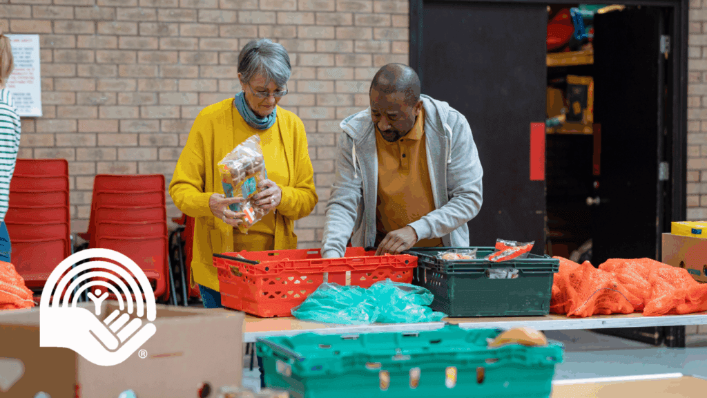 Group of volunteers organising food donations onto tables at a food bank in the North East of England. They are working together, setting up sections of the room in a church.