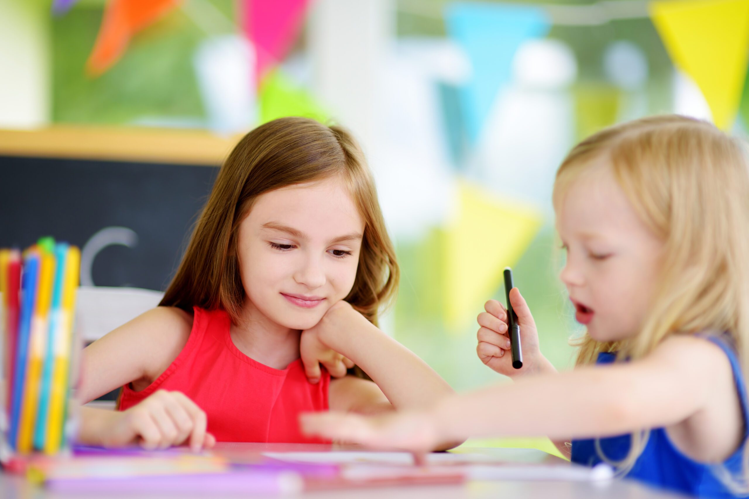 Two little sisters drawing with colorful pencils at a daycare. Creative kids painting together.